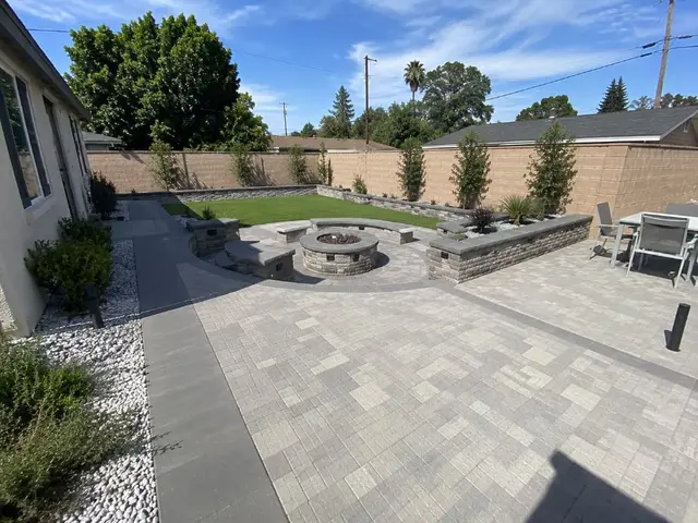 Curved backyard paver patio with retaining wall and landscape lighting