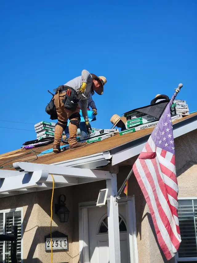 Worker installing roof shingles with American flag California